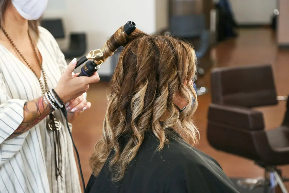 Coiffeuse réalisant des boucles sur une cliente aux reflets caramel