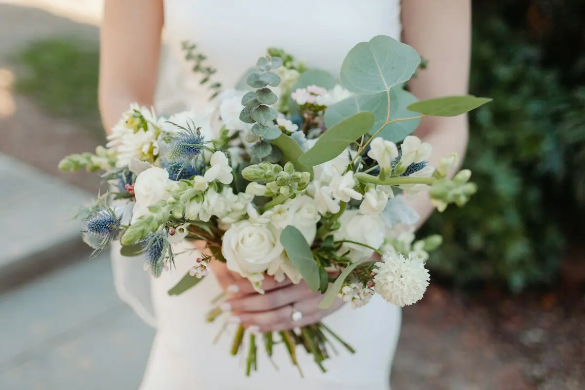 Bouquet de mariée blanc et vert tenu devant une robe