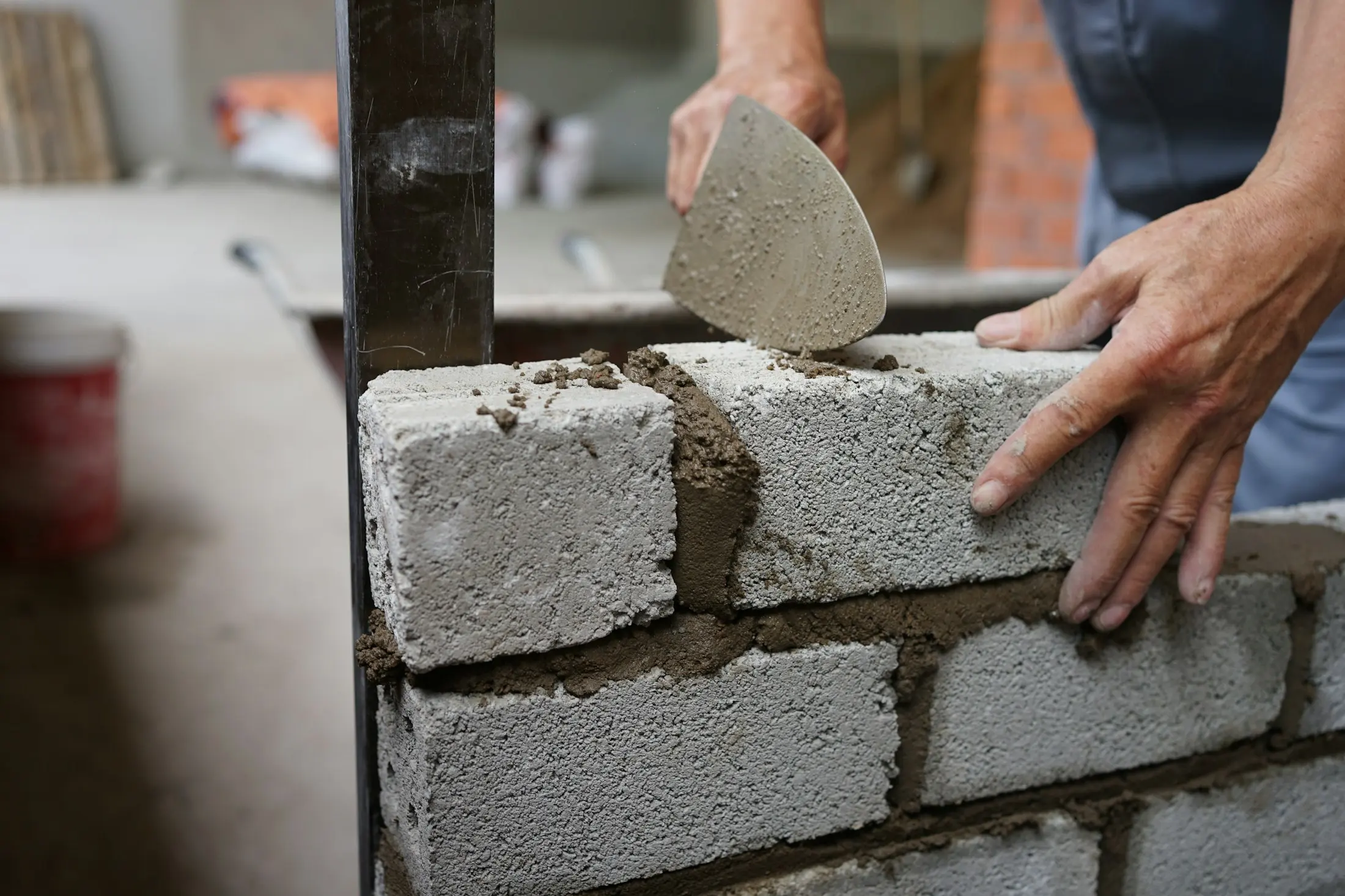 Mains de maçon posant du mortier sur un mur de parpaings