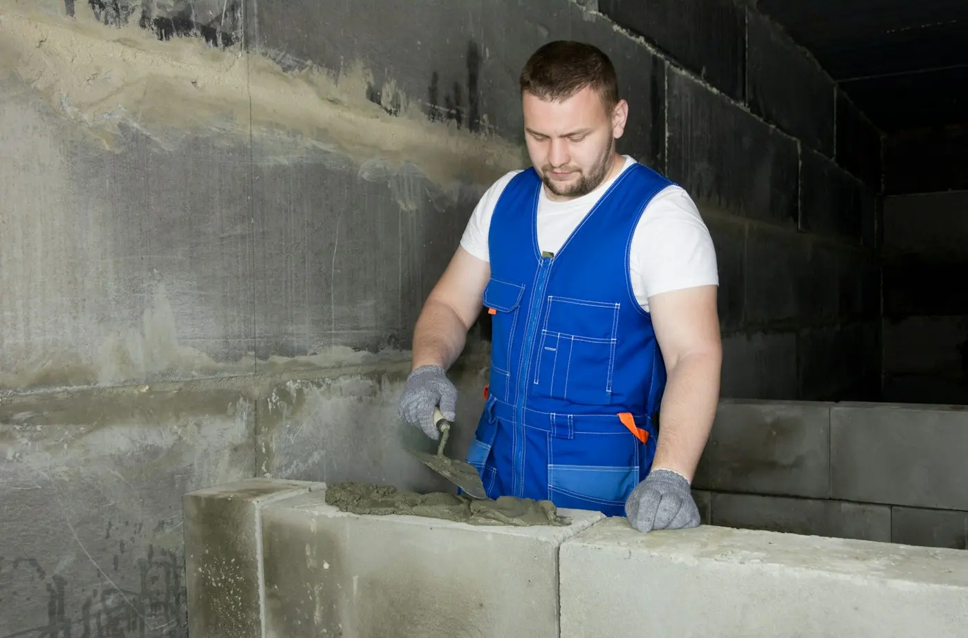 Maçon en gilet bleu montant un mur de parpaings