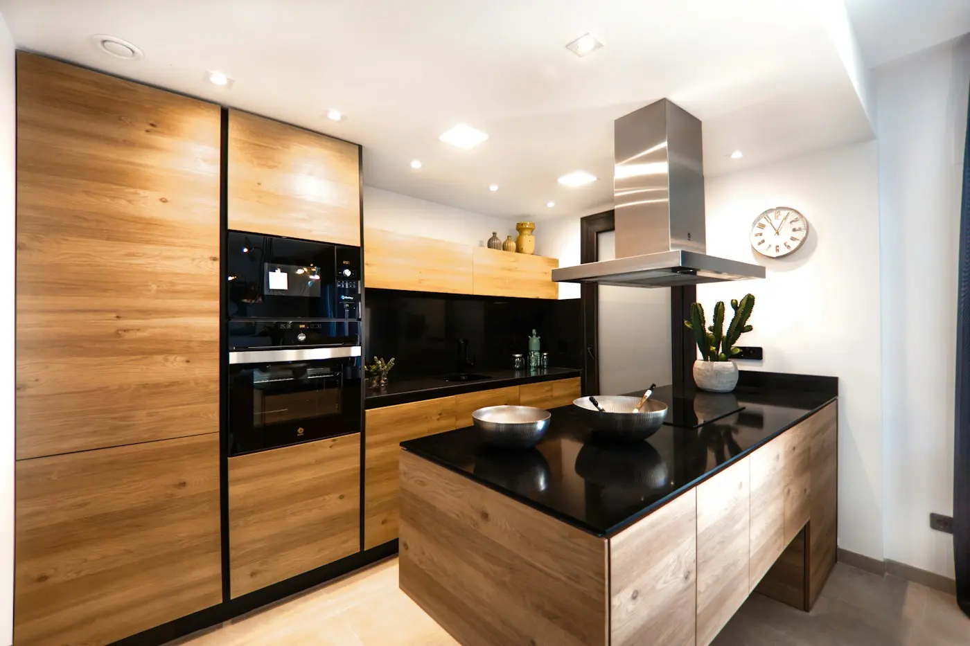 Cuisine en bois clair avec îlot noir et hotte inox