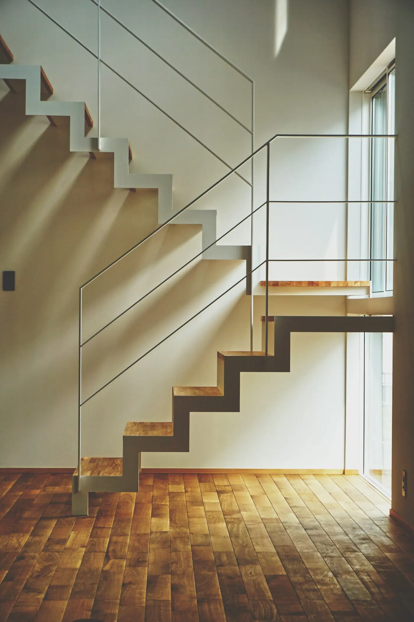 Escalier suspendu en bois clair le long d’un mur blanc
