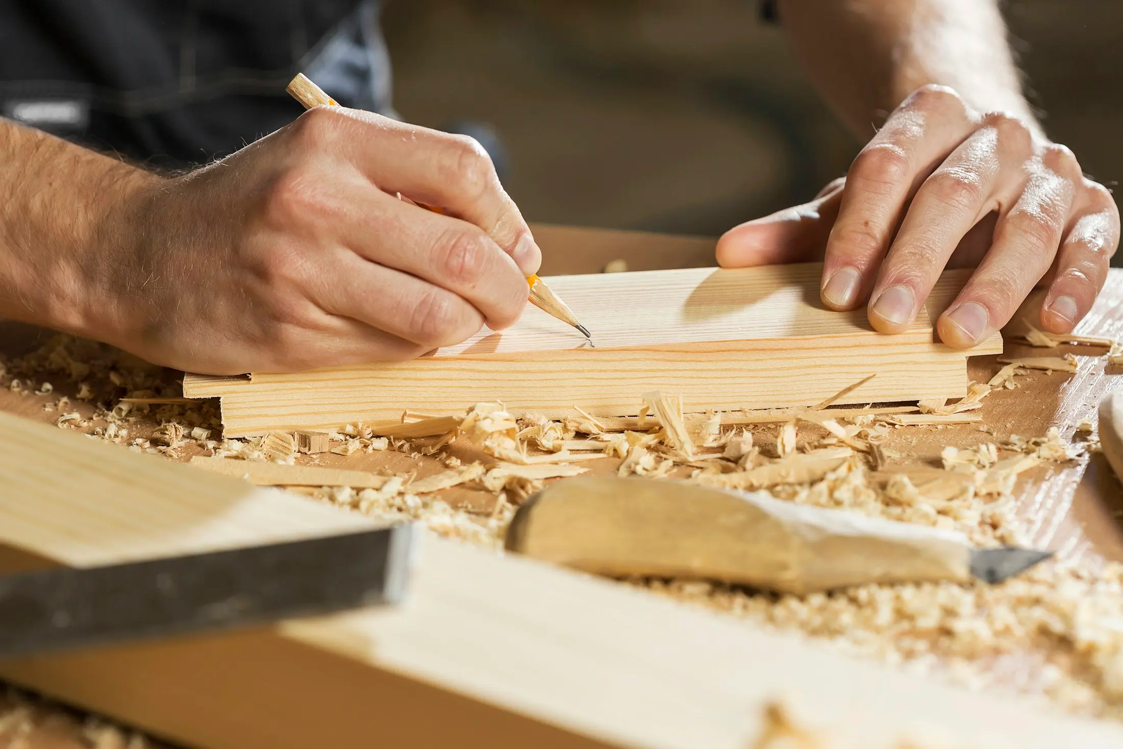 Menuisier traçant au crayon sur une planche, copeaux sur l’établi