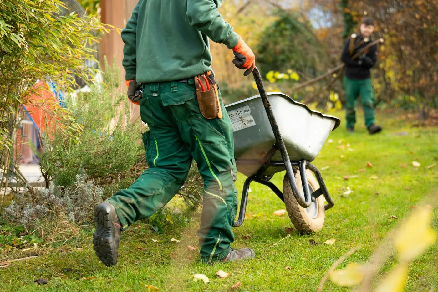 Jardinier poussant une brouette dans un jardin automnal