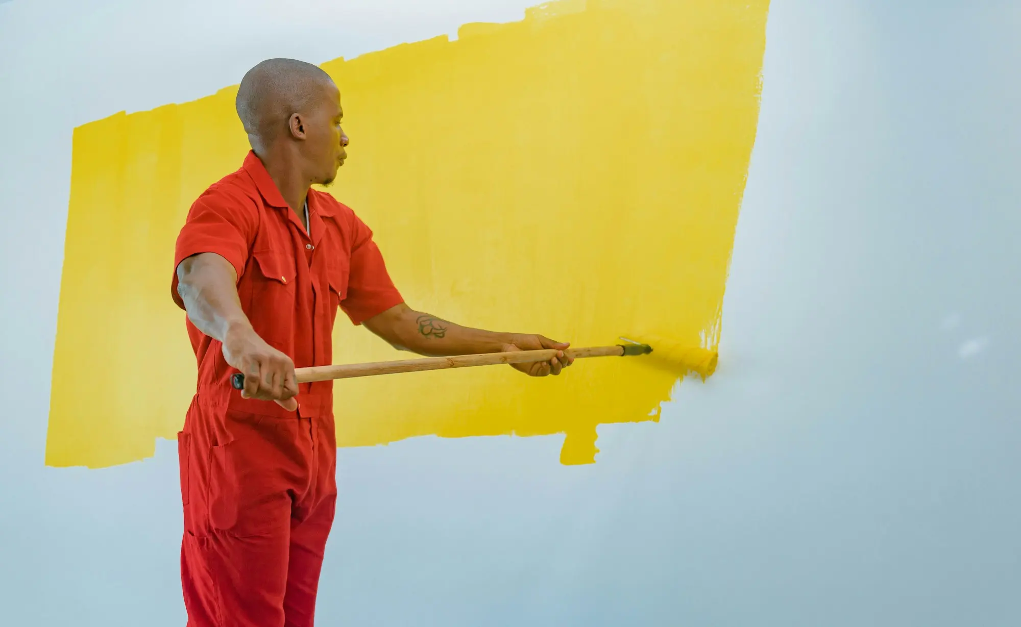 Peintre en combinaison rouge passant du jaune au rouleau sur un mur blanc