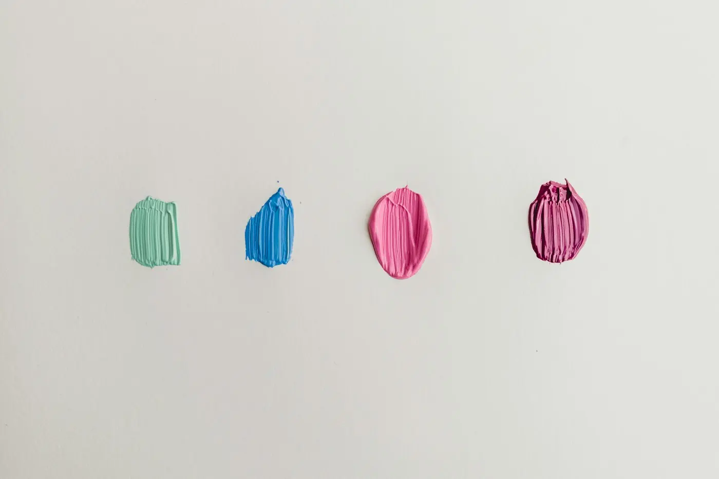 Quatre touches de peinture, vert, bleu et rose, sur un mur blanc