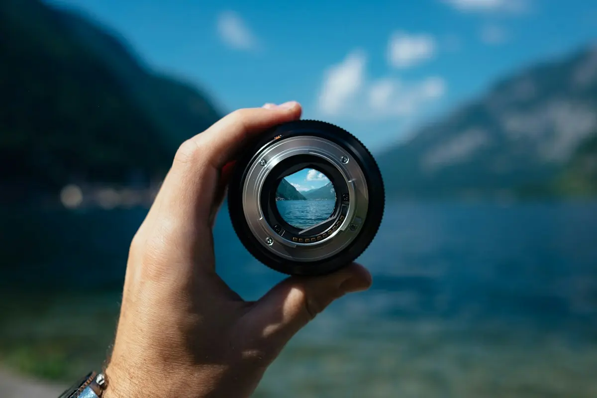 Objectif tenu à la main devant un lac et des montagnes