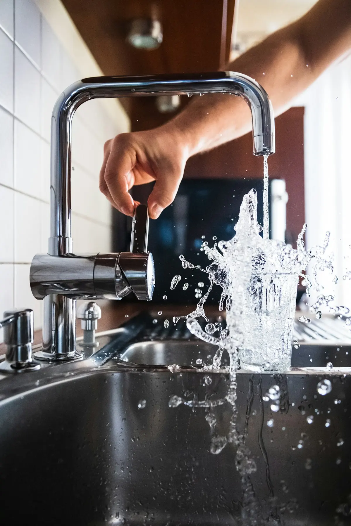 Main ouvrant un mitigeur de cuisine, eau qui jaillit