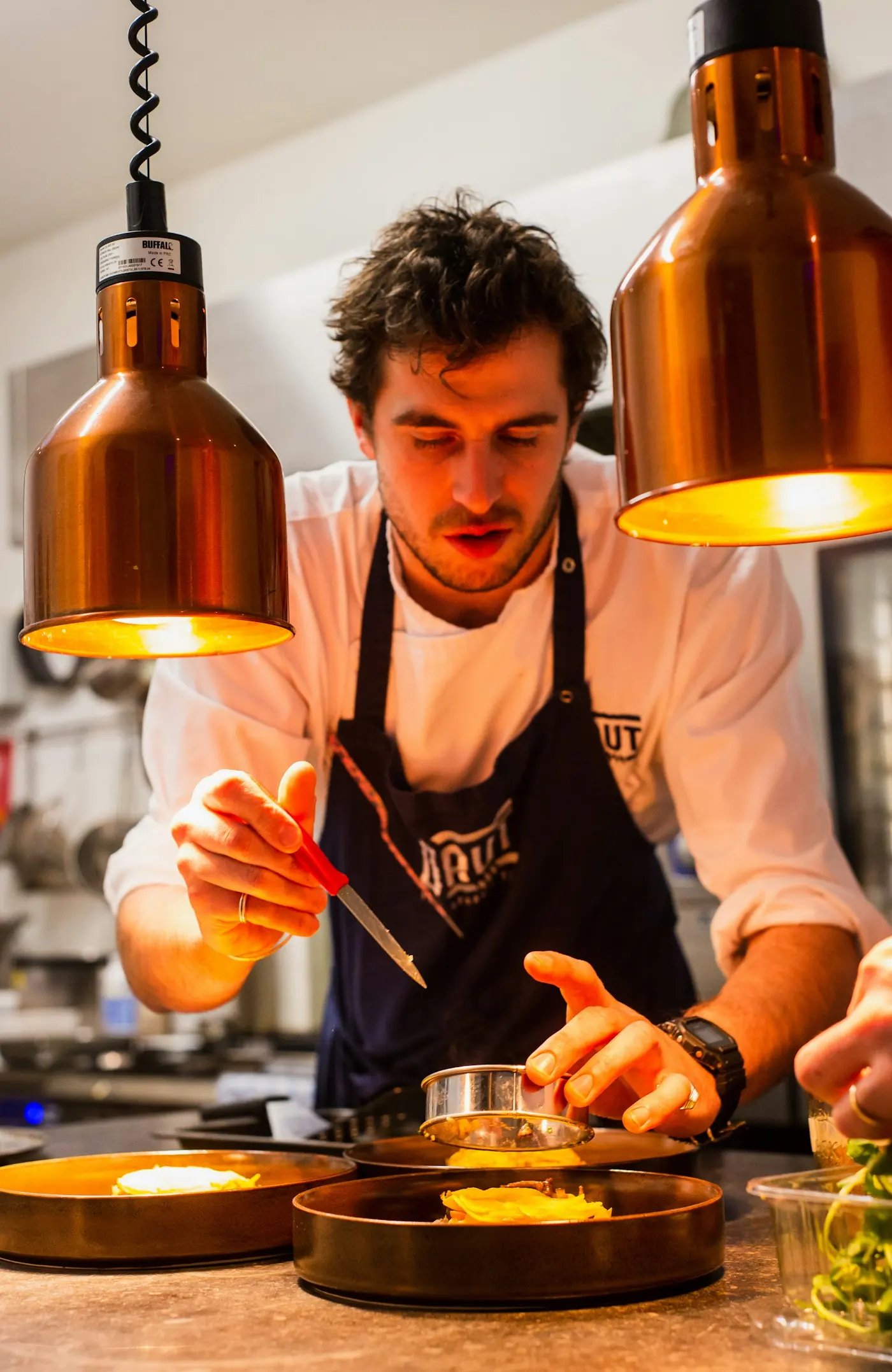 Chef concentré dressant une assiette sous des lampes en cuivre