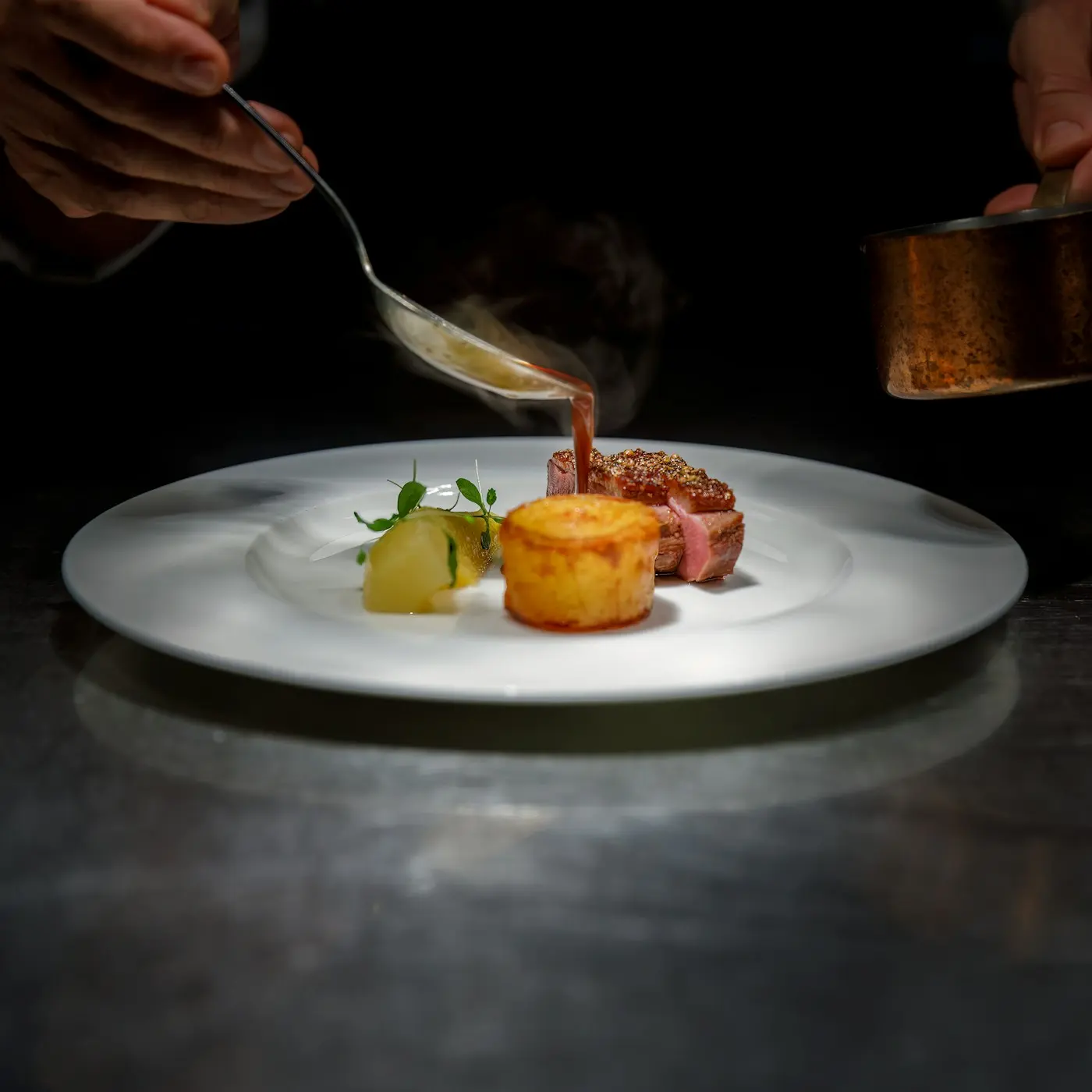 Chef nappant de sauce une pièce de viande dressée